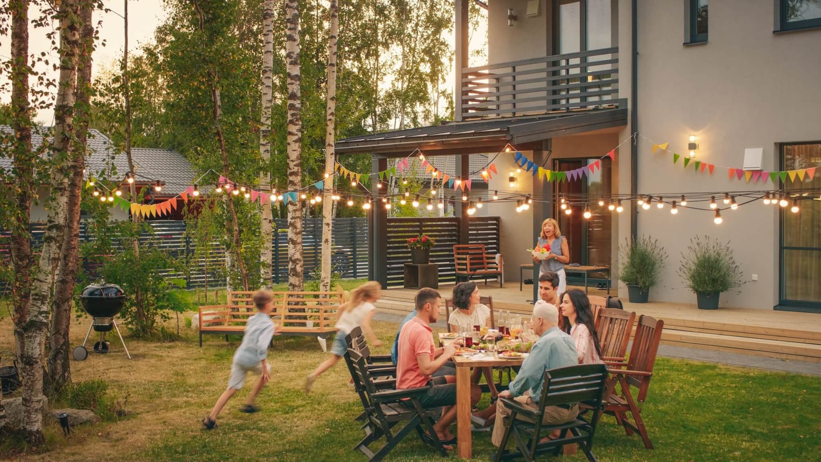 family enjoying a dinner party in their backyard while the kids run around the table