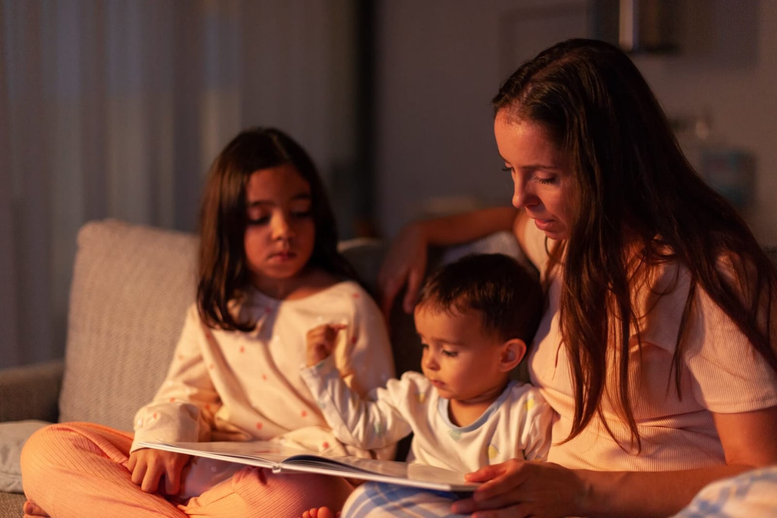 Mom telling a story to her children at night sitting on the couch