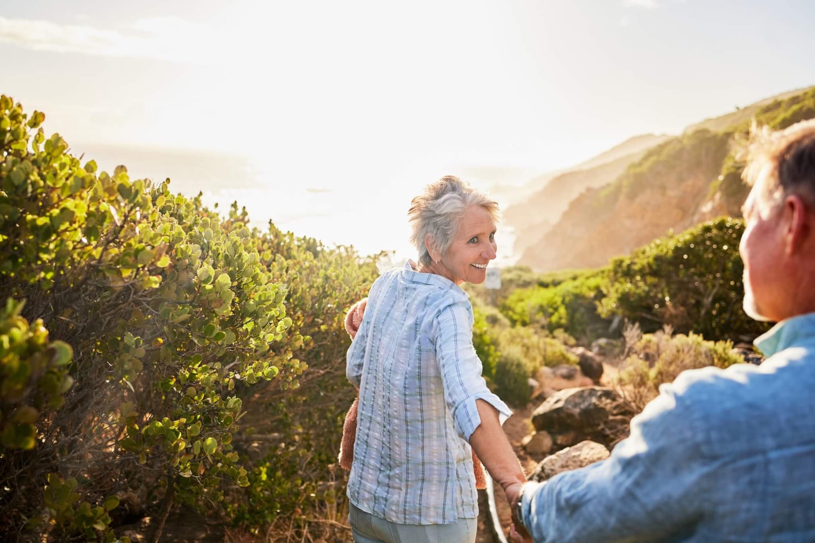 gracefully aging woman smiling back at her partner as they walk down a trail along a coastal cliff