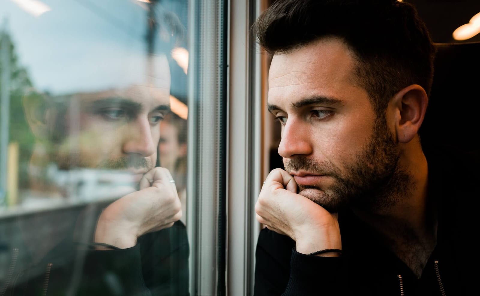 Young bearded man traveling by train in late afternoon