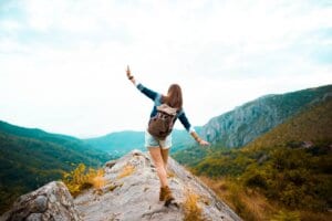 a woman balancing on a rock formation with her hands out as she's hiking - embracing women's health 20s image