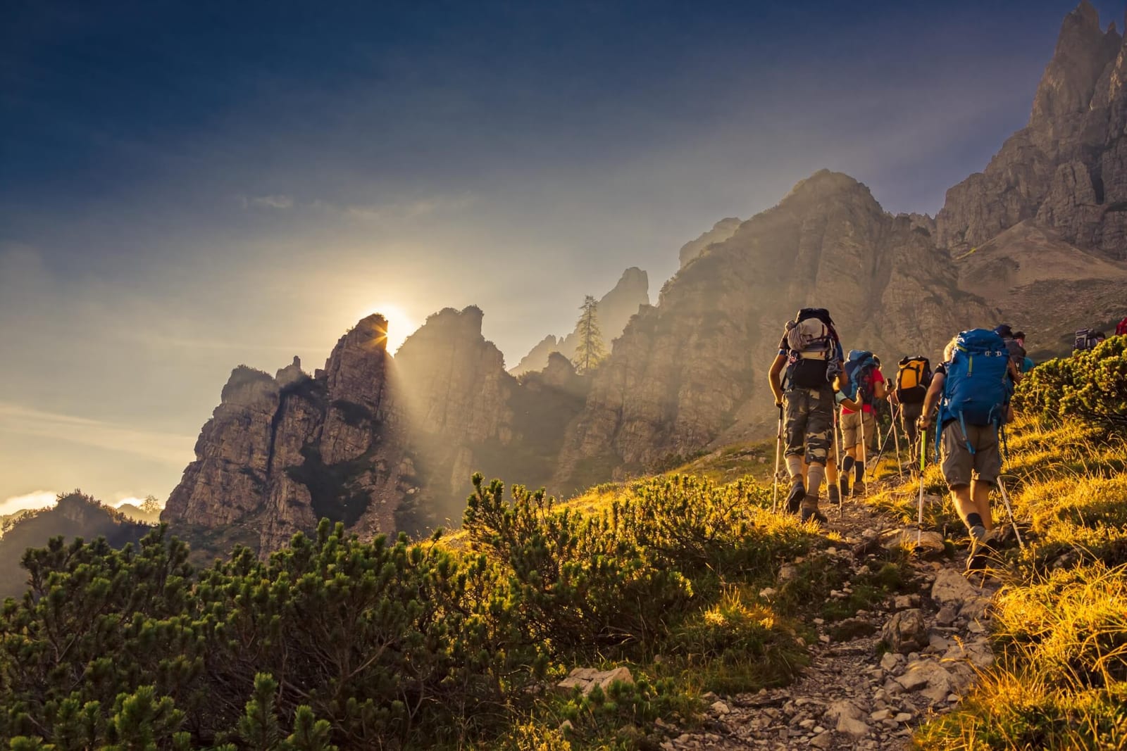 group of people hiking up a long mountain trail at sunrise