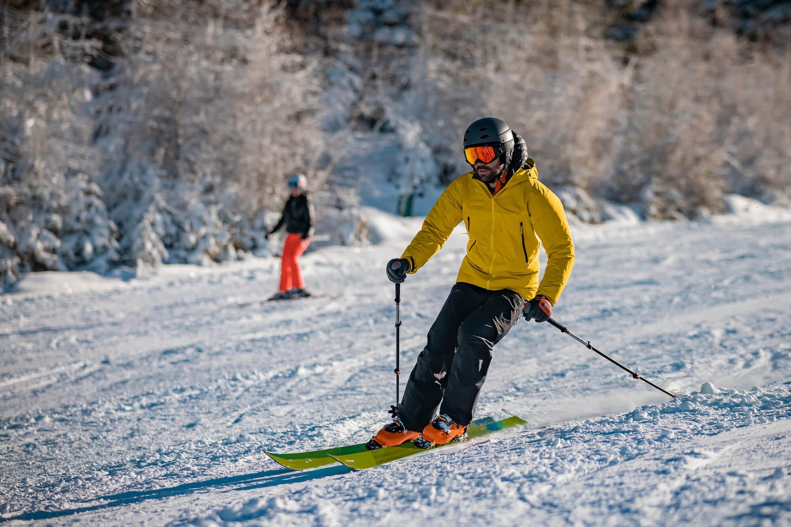 Young person in fashionable clothes is skiing past the camera on a ski slope on a sunny day. Carve or carving on ski piste, perfect weather, strong backlight.