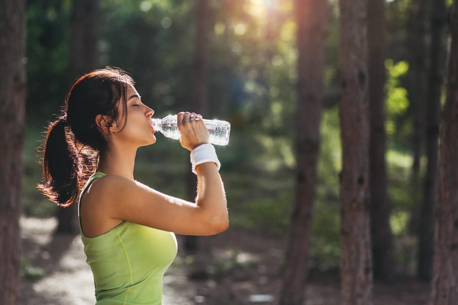 Girl drinking water from bottle in forest as part of taking care of your kidneys