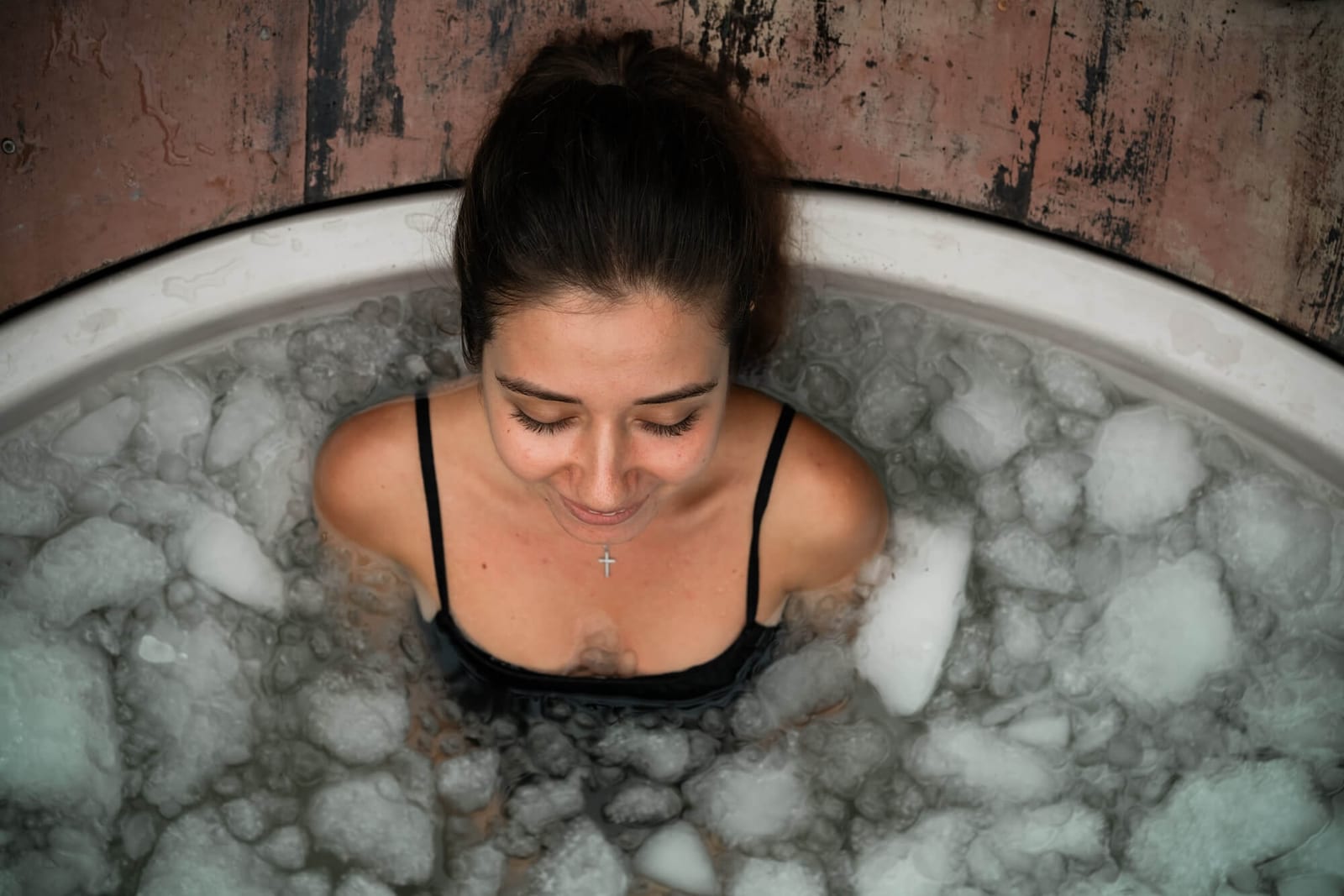 Woman practices cold therapy in an outdoor ice bath surrounded by tropical plants. A peaceful moment of self-care and healing