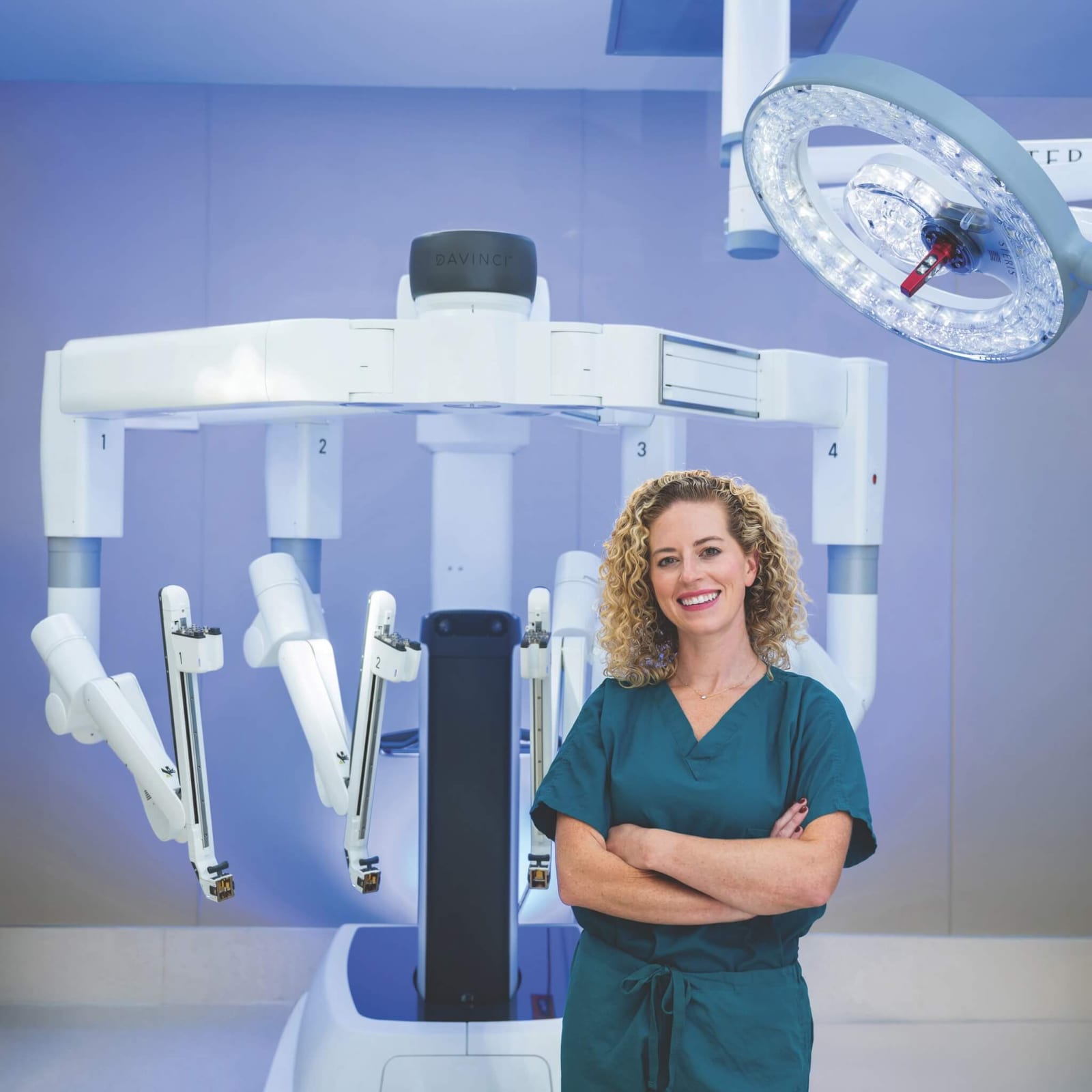 surgeon and gastroenterologist Dr. Alexandra Kovar standing in front of surgical machinery while wearing dark teal scrubs