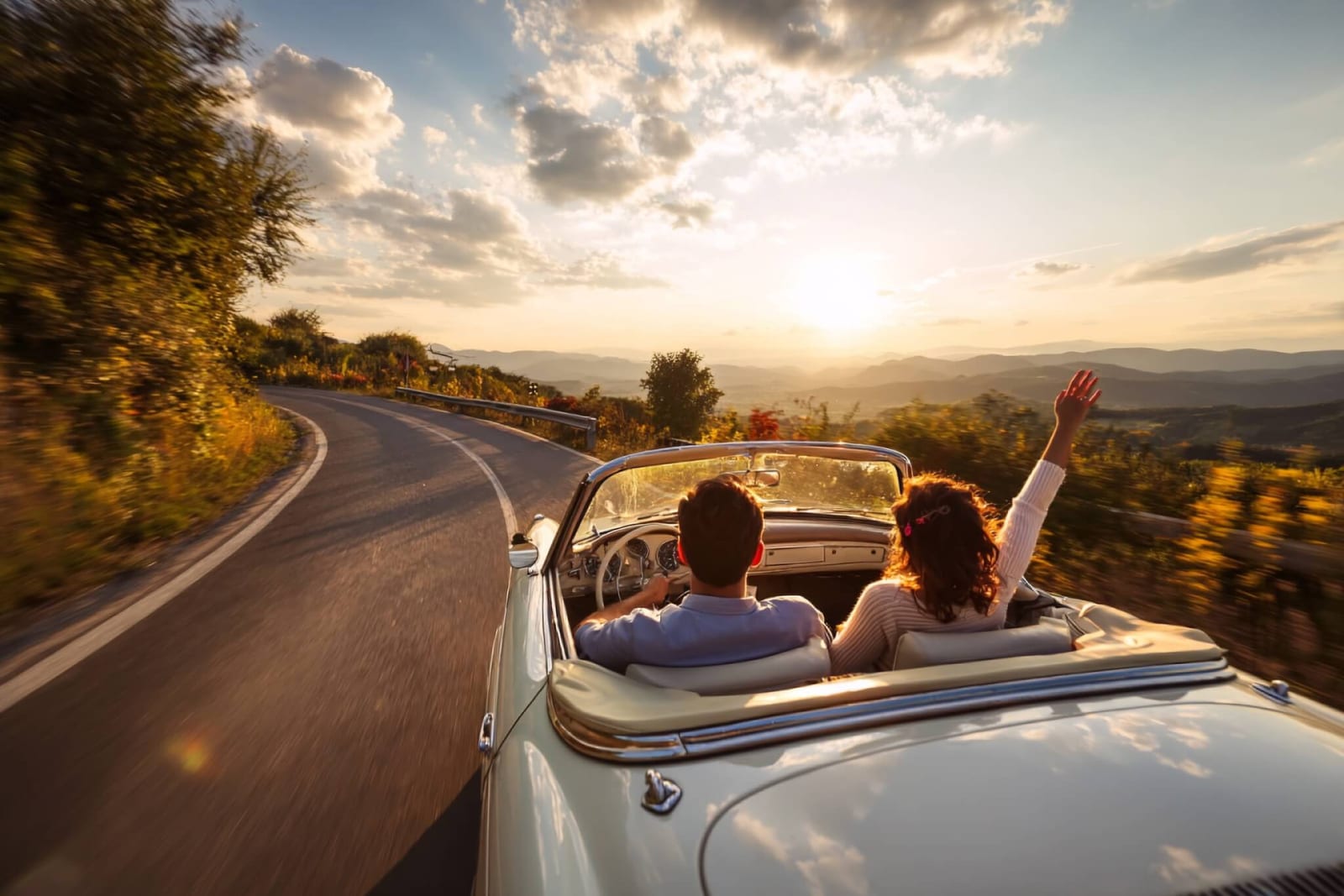 couple on a digital detox retreat driving their convertible on a winding mountain road at sunset