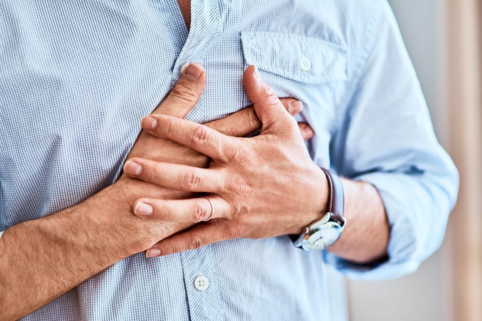 Shot of a unrecognizable man holding his chest in discomfort due to pain at home during the day.